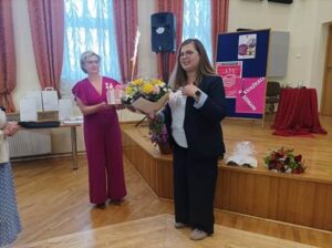 dwie członkinie DKK trzymają tor i kwiaty